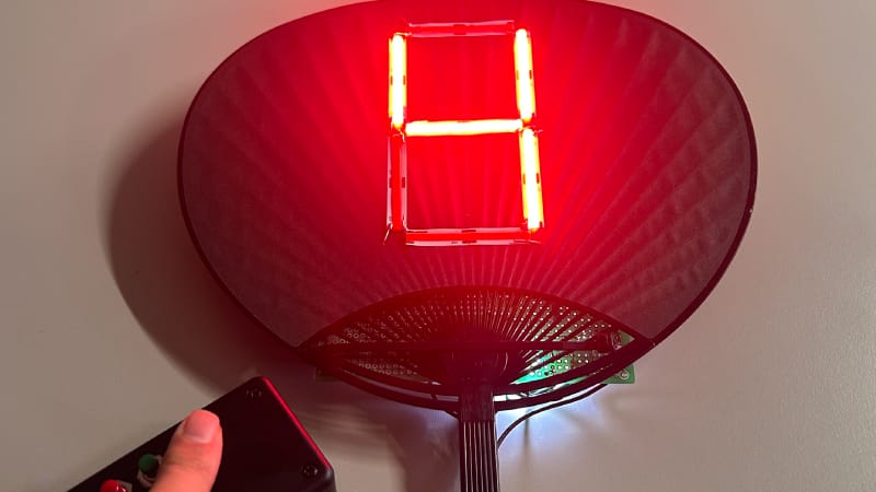 暗い駐車場で数字の4を赤く光らせるうちわ型LED表示器と、4色ボタンのリモコン